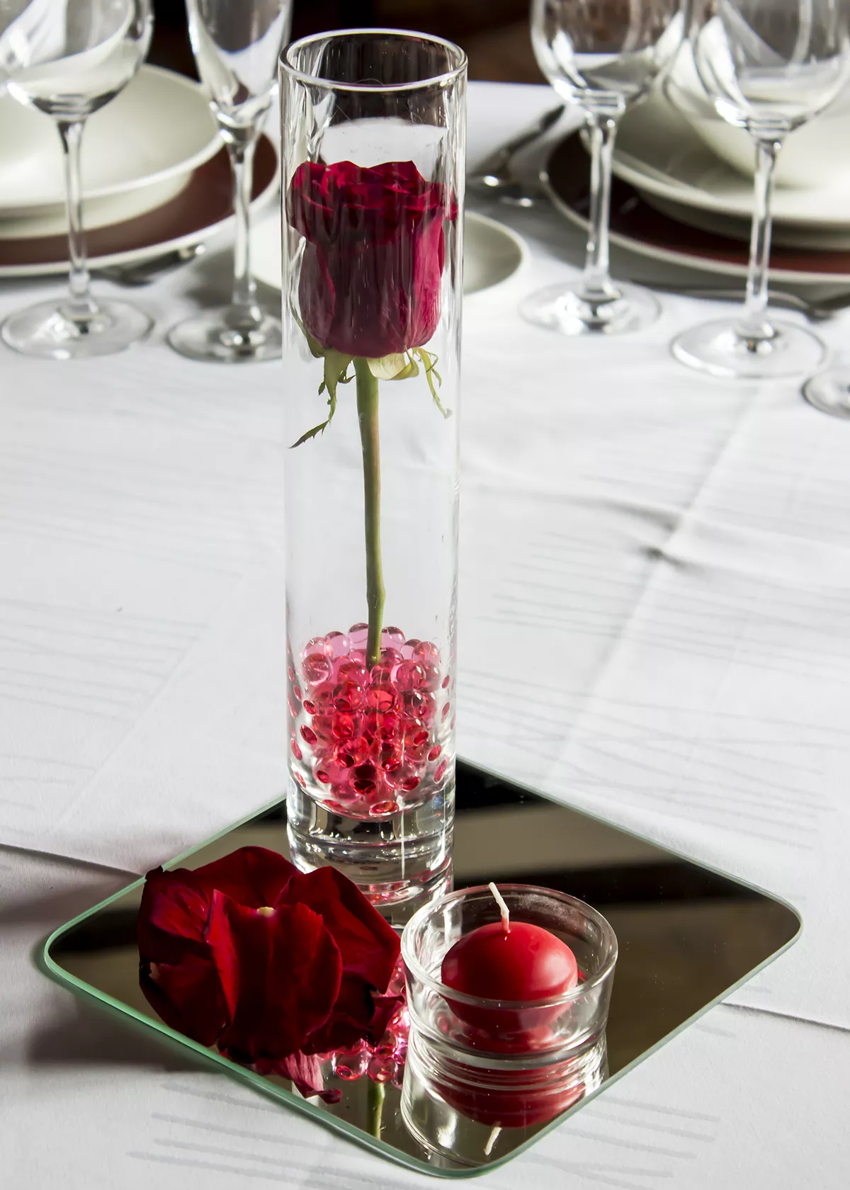 Centro de mesa con una rosa, una vela y pétalos de rosa, todo de color rojo