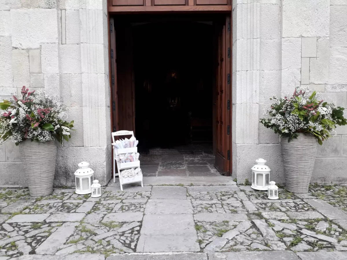 Entrada a una iglesia con flores a cada lado y una estantería con conos de pétalos